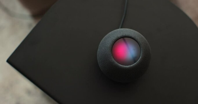Using an HomePod Mini speaker - the smart speaker is reacting to voice listening to human commands and signalling its attention by the changing lights. Concept of a smart home.
