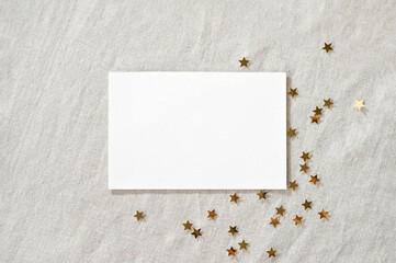 Blank paper card mockup and gold stars confetti on linen neutral beige background. Minimalist...