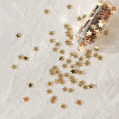 Obraz na płótnie Canvas Gold star confetti sparkle scattered from bottle on neutral beige linen texture background. Minimalist aesthetic festive party celebration concept