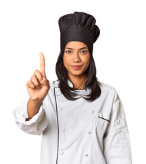 Young Filipina chef with cooking hat in studio showing number one with finger.