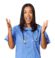 Young Filipina nurse posed in studio receiving a pleasant surprise, excited and raising hands.