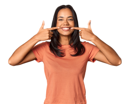 Young Filipina with long black hair in studio smiles, pointing fingers at mouth.