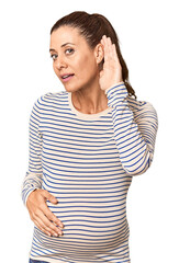Pregnant middle-aged woman in studio setting trying to listening a gossip.