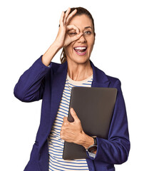 Middle-aged entrepreneur with laptop in studio excited keeping ok gesture on eye.