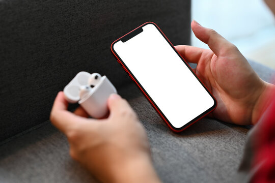 Young man holding earphones box and using smartphone on sofa