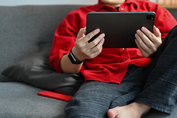 Relaxed young man sitting on couch and browsing internet or watching social media videos on digital tablet