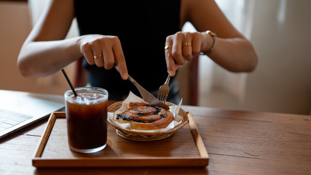 Close-up image of a woman eating a yummy croissant roll, and iced coffee in a cafe.