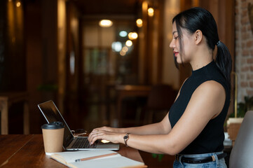 Side view of a beautiful Asian businesswoman is working on her laptop in a coffee shop.