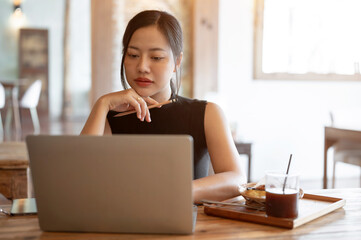 A confident and thoughtful Asian woman is reading online articles while sitting in a coffee shop.