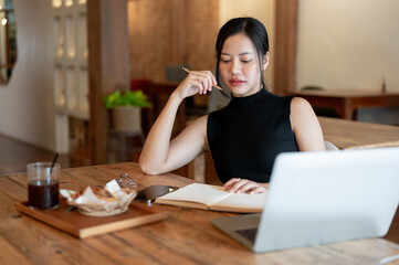 A thoughtful and gorgeous Asian woman focuses reading a book while working remotely in a cafe.