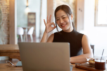 A businesswoman is joining an online meeting, showing the Okay hand sign, working at a cafe.