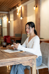 An attractive young Asian woman is using her smartphone while sitting in a coffee shop.