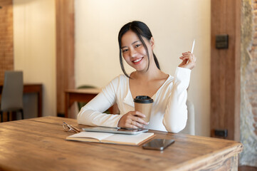 A beautiful Asian woman sits at a table in a beautiful coffee shop with a coffee cup in her hand.