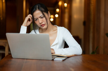 A stressed Asian woman is staring at her laptop screen with an unsatisfied face, having a problem.