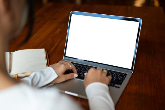 Close-up image of a woman working on her laptop at a table indoors. A white-screen laptop mockup