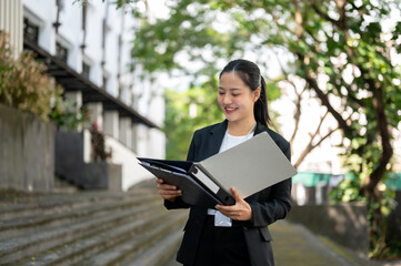 An attractive Asian businesswoman is checking her document in a binder while walking in the city.