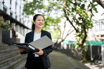 Fototapeta premium A successful Asian businesswoman is standing with binders in her hands outside of the building.