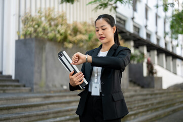 A busy Asian businesswoman is checking time on her wristwatch while walking in the city street.