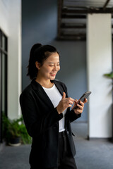 A businesswoman is texting someone on her smartphone while standing in her company corridor.