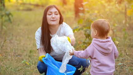 Toddler girl contributes to environmental conservation by helping mom in cleaning up litter. Child helps mother to pick up garbage, sunlight