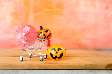 Halloween pumpkin lantern in shopping cart and pink paper umbrella with space on blurred background, Halloween decoration item shopping