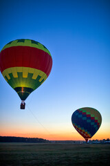Two Colorful Air Balloons Levitating Over the Ground Outdoors Against Clear Blue Skies At Twilight.