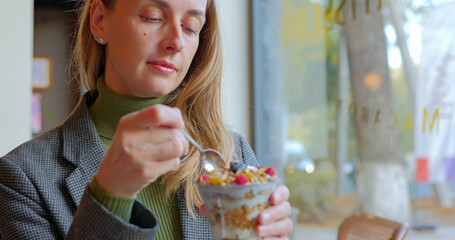 Woman eating natural organic berry smoothie bowl with various nuts in vegan cafe