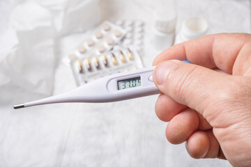 Hand holding a digital thermometer and pills on a white background.