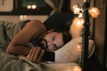 Young man with phone in bed in the evening. Evening leisure at home