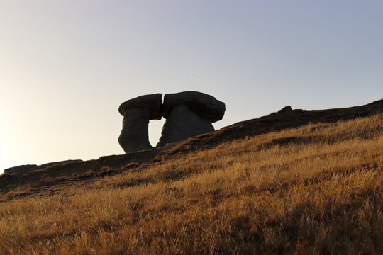 Two mountain stones resembling ETs look like they kiss each other at sunset profiled on cliff against completely clear sky