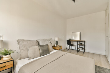 a bedroom with a bed, desk and mirror on the wall next to the bed is a small wooden table