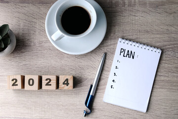 Happy New Year concept. Wooden cube with the number 2024 with notebook plan and coffee on office desk.