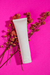 White skin care bottle package on dried flowers on pink background.
