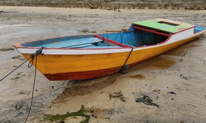 an orange fishing boat rests on a receding beach