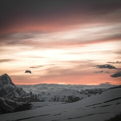 a pink, orange and purple sky with clouds over snowy mountains