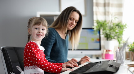 Portrait of happy smiling child with mother having music time together. Joyous girl sitting near mom and looking at camera with gladness. Parenthood and childhood concept