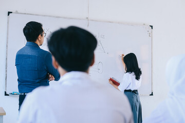 Male Asian teacher watching student writing math exercise on white board