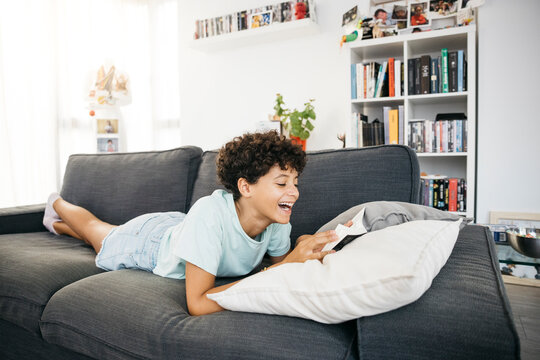 Ten years old girl lying on a sofa and reading a book in a living room.