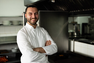 Portrait of smiling caucasian male chef with arms crossed standing in kitchen at cooking school