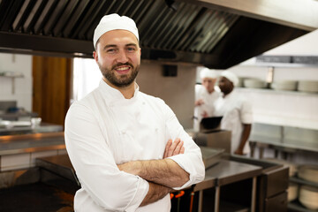 Portrait of smiling caucasian male chef in white uniform standing in kitchen at cooking school