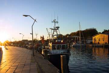 Promenade and fishing boat at the port of the charming coastal town of Eckernförde at sunset with sunrays.