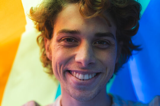 Portrait of happy caucasian man covered with lgbt flag at home