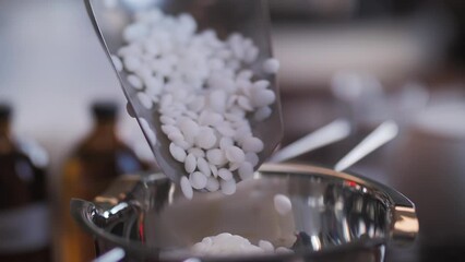 A metal measuring spoon pours soy wax into a metal pot, making candles