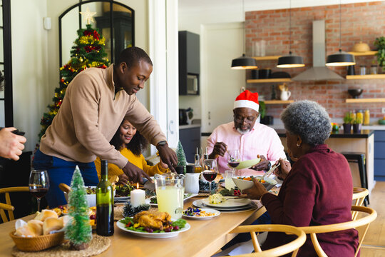 Happy african american family having christmas dinner in decorated dining room at home