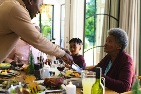 Happy african american family having christmas dinner in decorated dining room at home