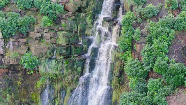 Yorkshire Moors' picturesque waterfall, aerial video depicts water flowing over large rocks into a deep blue pool, hikers below.