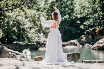 a beautiful woman in a long white dress looks into the distance at a beautiful lake with swans rear view