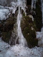 Icy frozen winter waterfall in a mossy forest