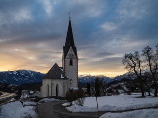 Fototapeta na wymiar Winter sunset landscape of an old austrian church in an alps village, snowy mountains, Wallfahrtskirche Maria Schnee Matzelsdorf