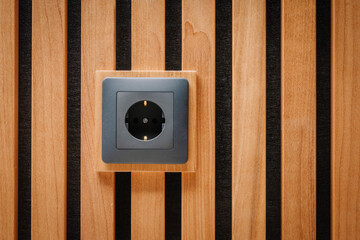 Black outlet plug on the wooden wall. Socket and European Power in the New Flat. Acoustic fluted wood panel.